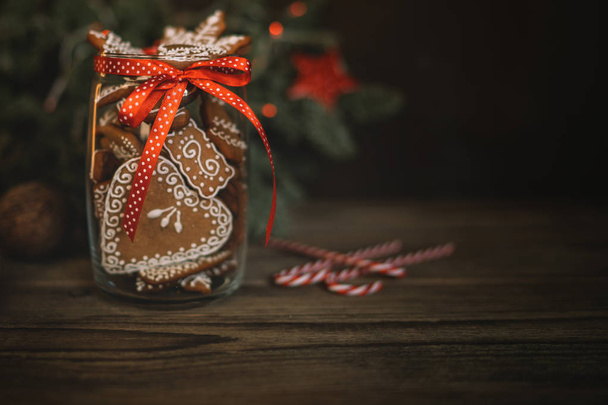 Christmas gift with homemade gingerbread cookies, nuts and chocolates. Glass jar, fir branches, Christmas spices and decor. Winter holidays, New Year or Christmas concept. Toned image. Soft focus. - Foto, afbeelding