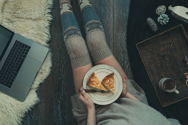 Woman eating cake at Christmas eve. Girl holding plate of christmas cake relaxing at home, drinking cacao, using laptop. Winter and Christmas holidays concept. Top view. Soft, comfy lifestyle. - Foto, Imagen