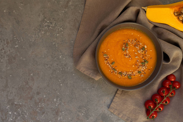 Seasonal autumn food. Spicy pumpkin ans carrot soup with cream and seasoning in rustic bowl on dark gray background. Hot, fresh vegetable soup. View from above with copy space. Toned image. - Valokuva, kuva