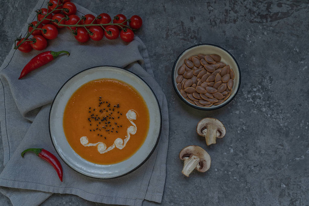 Bowl of pumpkin organic soup with cream and pumpkin seeds on gray background. Dietary vegetarian food. Concept of healthy eating food. Homemade autumn soup. Top view with copy space. Toned image. - Photo, image