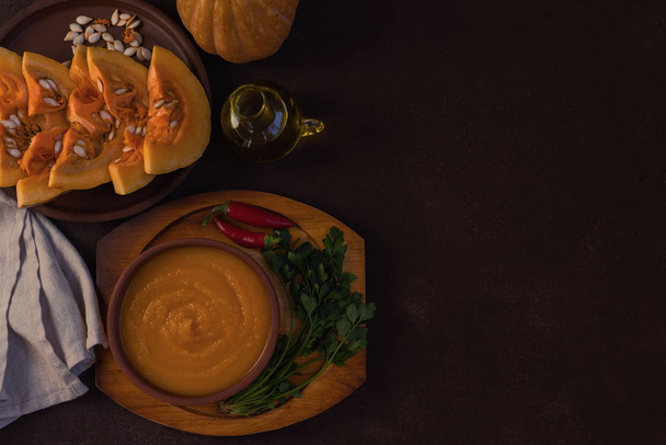 Traditional fall dishes, hot and spicy pumpkin soup with pumpkin seeds and cream on gray stone table. Autumn dinner. Organic vegetables and healthy food concept. Top view with copy space. Toned image - Photo, Image
