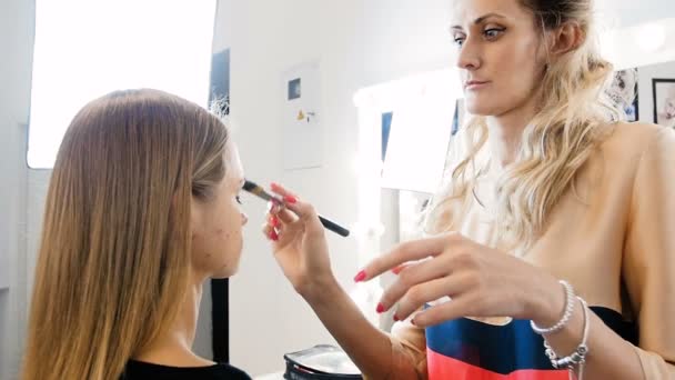 Closeup vídeo em câmera lenta do artista de maquiagem profissional aplicando cosméticos e preparando o jovem modelo feminino para fotografar
 - Filmagem, Vídeo