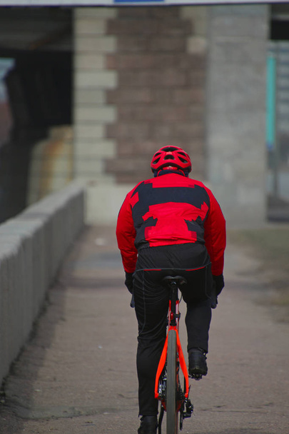 Kerékpáros egy piros melegítőben lovagol mentén rakparton  - Fotó, kép