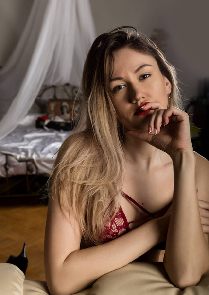 seductive young woman in red bra resting on sofa at hotel room. sexy hipster girl enjoying on the couch - Foto, Imagem
