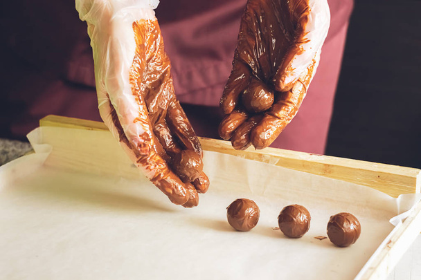 Φτιάχνω χειροποίητες σοκολάτες. Στρογγυλές σοκολάτες περιπορισμένες με υγρή σοκολάτα στην επιφάνεια του τραπεζιού. Επιλεκτική εστίαση. - Φωτογραφία, εικόνα