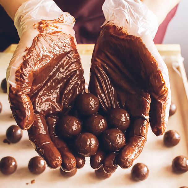 Making handmade chocolates. Round chocolates doused with liquid chocolate in the hands of the confectioner chocolatier. - Photo, Image
