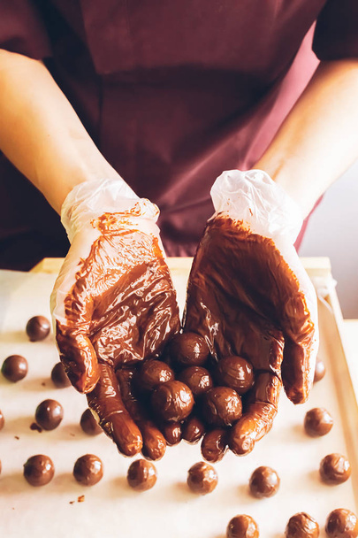 Hacer chocolates hechos a mano. Chocolates redondos rociados con chocolate líquido en las manos del chocolatero confitero
. - Foto, Imagen