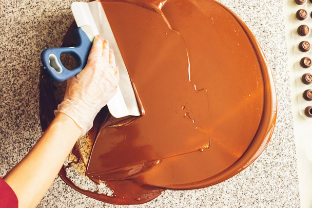 Виготовлення шоколадних цукерок ручної роботи. Кондитер наливає на поверхню рідкий темний шоколад. Крупним планом. Вибірковий фокус
. - Фото, зображення