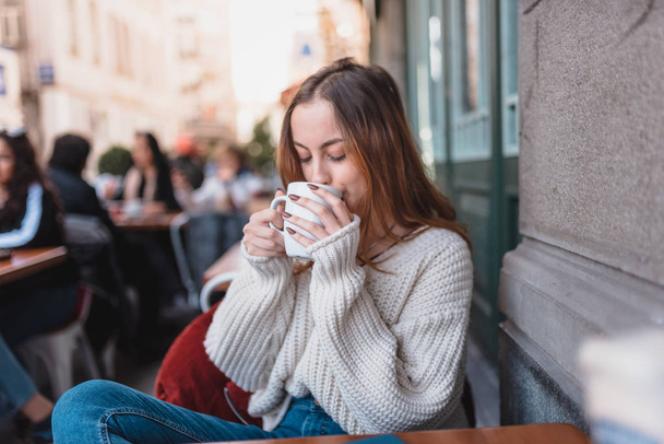 Beautiful young girl in outdoor cafe drinks coffee - 写真・画像