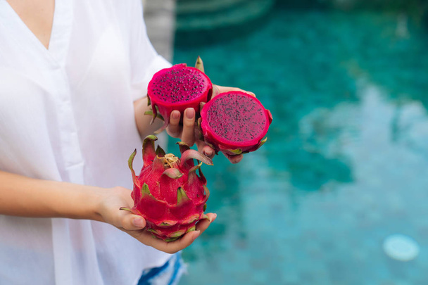 Close up of woman hands holds dragon fruit with blurred pool on background - Photo, image