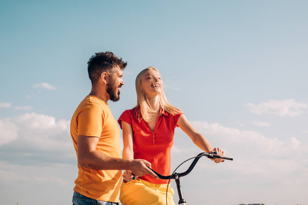 Summer woman with retro bike on blue sky background. Happy loving couple. Greatest Love Stories. Couple in summer dress rides a bike. Couple with vintage bike. - Fotó, kép