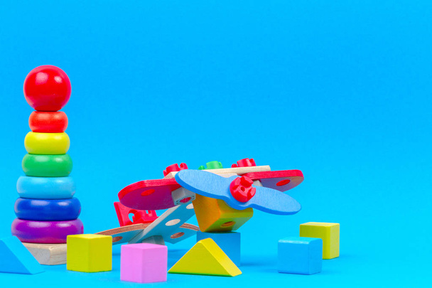 Baby kid toy background. Wooden toy plane, baby stacking rings pyramid and colorful blocks on blue background - Photo, image