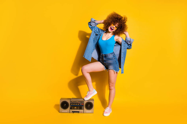 Full length body size photo funny funky she her lady wavy styling curls leg stand on old-fashioned tape recorder wear specs casual jeans denim shirt shorts tank top clothes isolated yellow background - Foto, Imagen