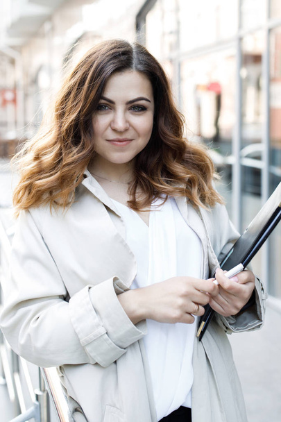 A young, sympathetic woman, not a thin-headed body building, holds a folder of paper in her hands. Happy young business woman with a folder at the office building in her hands - Fotografie, Obrázek