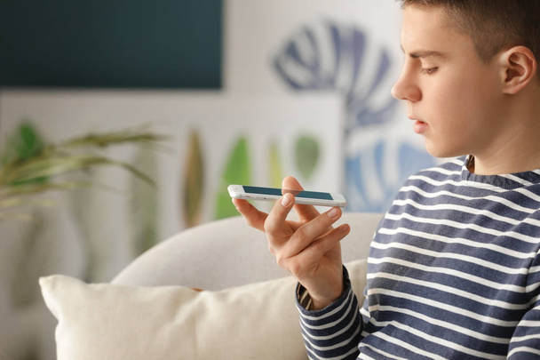 Teenage boy with mobile phone in room. Modern technology and smart home automation - Φωτογραφία, εικόνα