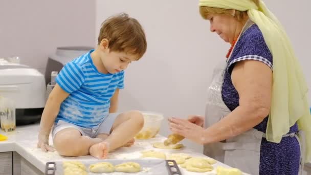 Lähikuva onnellinen hymyili isoäiti ja pojanpoika vaivaamalla tytär yhdessä. vanhuksen ja pienen pojan hidas liike valmistamassa pastaa tai pizzaa yhdessä
. - Materiaali, video