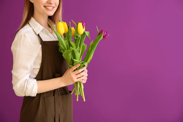Young female florist with bouquet on color background - Foto, Imagem