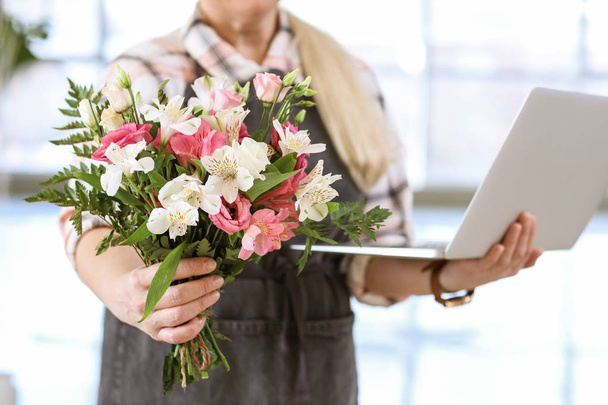 Florist with laptop and beautiful bouquet in shop - Фото, изображение