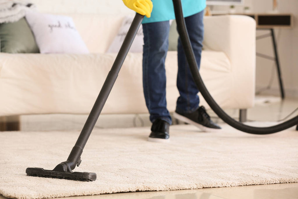 Male janitor hoovering carpet in flat - Foto, imagen