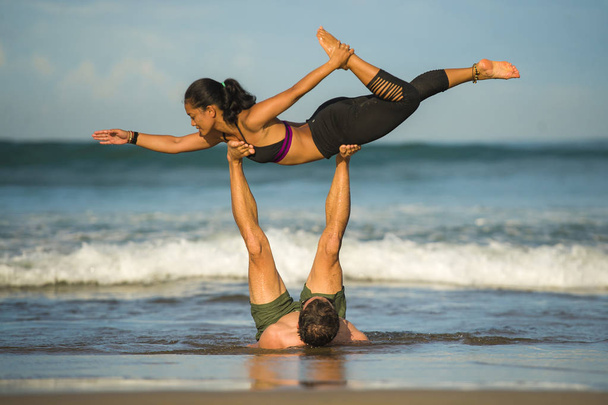 молодая привлекательная и концентрированная пара акробатов практикующих баланс акро-йоги и упражнения для медитации на прекрасном пляже под голубым небом в уме и контроле над телом
 - Фото, изображение