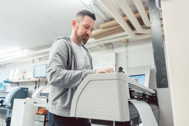 Mann bereitet Großformatdrucker für Druckauftrag vor - Foto, Bild