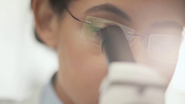Selektiver Fokus eines afrikanisch-amerikanischen Wissenschaftlers in einer Brille unter dem Mikroskop mit Sonnenlicht auf dem Hintergrund - Filmmaterial, Video