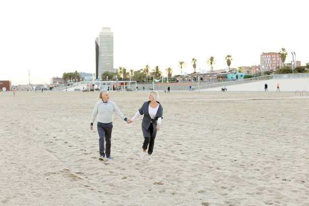 Senior happy husband and wife running on sand beach and holding hands. - Photo, Image