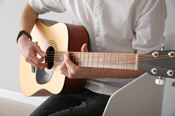 Komea nuori mies soittaa kitaraa sisätiloissa
 - Valokuva, kuva