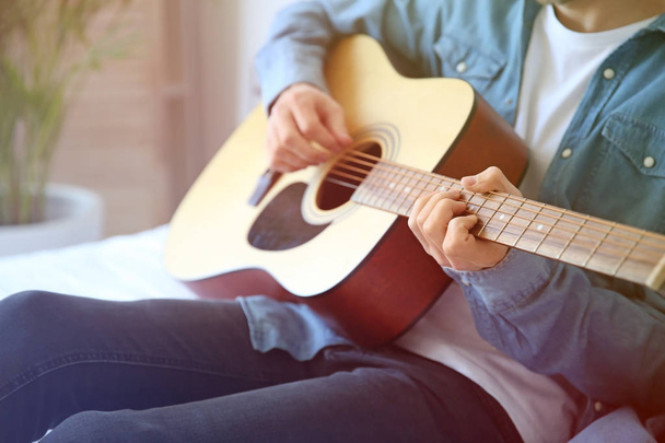 красивый молодой человек играет на гитаре дома - Фото, изображение