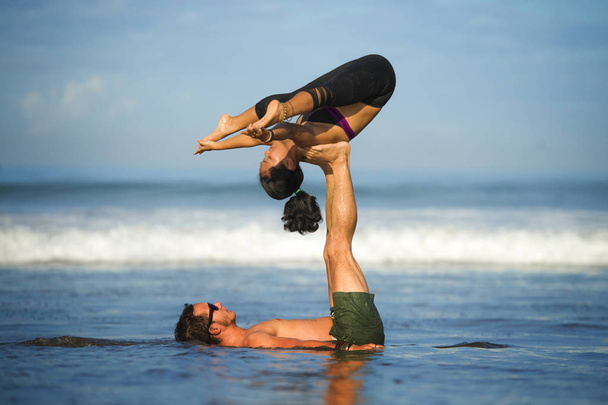 outdoors lifestyle portrait young attractive and concentrated couple of yoga acrobats practicing acroyoga balance and meditation exercise on beautiful beach - Valokuva, kuva