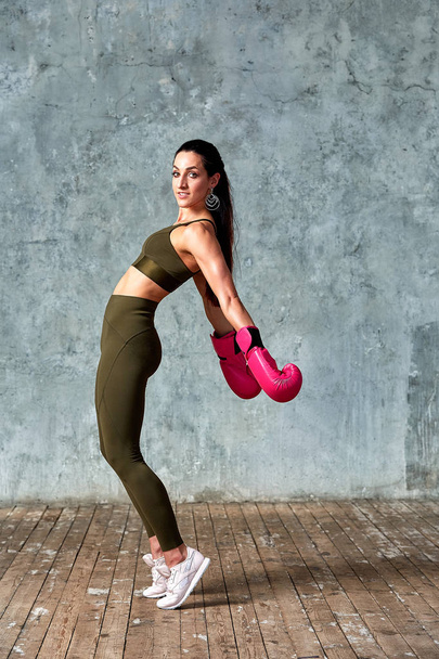 Beautiful athletic girl posing in pink boxing gloves on a gray background. Copy space. Concept sport, fight, goal achievement. - Fotografie, Obrázek