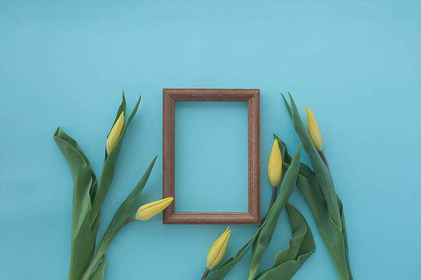 wooden frame with yellow tulips on blue textural background. Fla - Foto, afbeelding