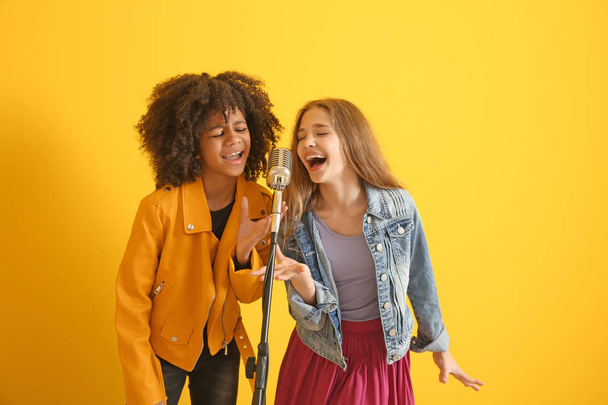 Teenage girls with microphone singing against color background - Фото, изображение