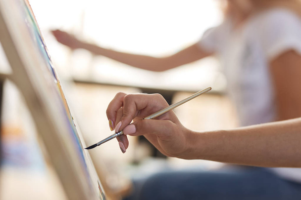 Girls hand holds a paint brush. Process of painting picture at the easels in the art studio - Foto, Imagen