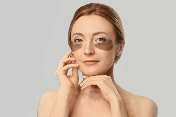 Volwassen vrouw met onder-oog patches op lichte achtergrond - Foto, afbeelding