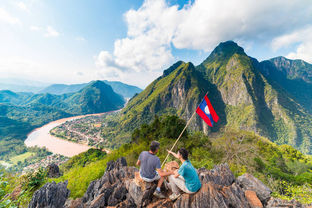 Pár na vrcholu hory v Nong Khiaw panoramatickém pohledu přes údolí řeky Nam ou Laosu národní vlajky malebná horská krajina slavné cestování v jihovýchodní Asii - Fotografie, Obrázek