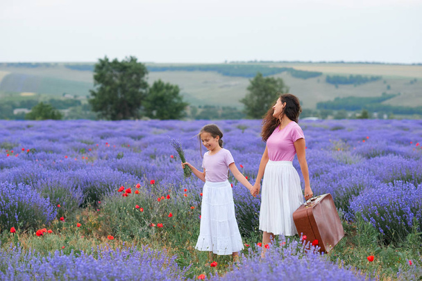 young woman and girl are walking through the lavender flower field, beautiful summer landscape - Photo, Image