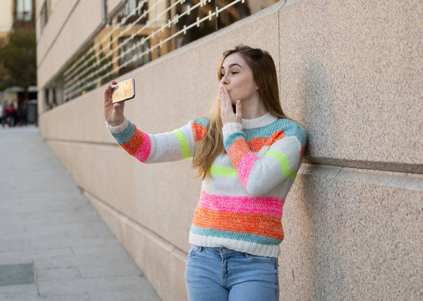 Happy pretty teenager girl using smart mobile phone excited blowing a kiss and waving to followers friends or family recording video or chatting. Video call In technology Communications and Blogging. - Foto, afbeelding