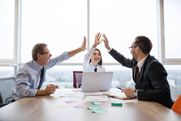 Um grupo de colegas de negócios dando uns aos outros high-five e sorrindo enquanto trabalhava no escritório
 - Foto, Imagem