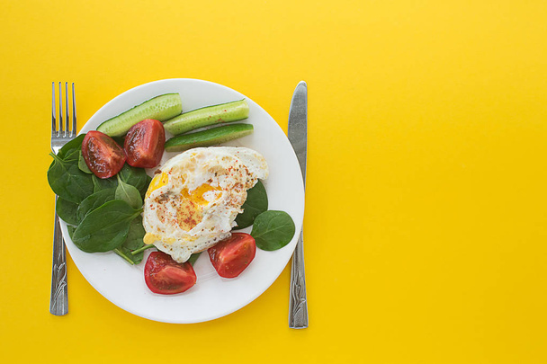 breakfast fried egg and spinach on a plate on a yellow background. Vegetables. Flat lay, copy space, top view. - Фото, изображение