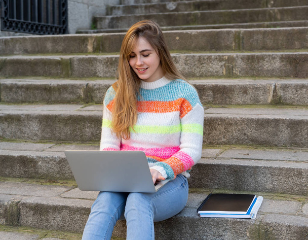 Attractive trendy teen student or young college girl working on laptop on the internet, blogging, chatting and checking email on steps in a european city. In Student learning online City lifestyle. - Fotografie, Obrázek