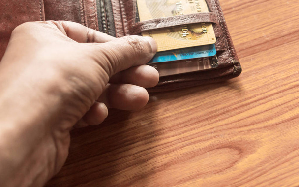 Рука людини витягає кредитну картку з грошової сумочки. Зображений зблизька. Дерев "яний стіл. - Фото, зображення