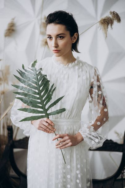 attractive woman posing in white dress and holding green leaf  - Fotografie, Obrázek