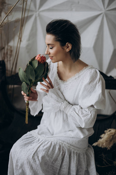  woman  smelling exotic flower while sitting on the wooden bench, studio shot - Foto, immagini
