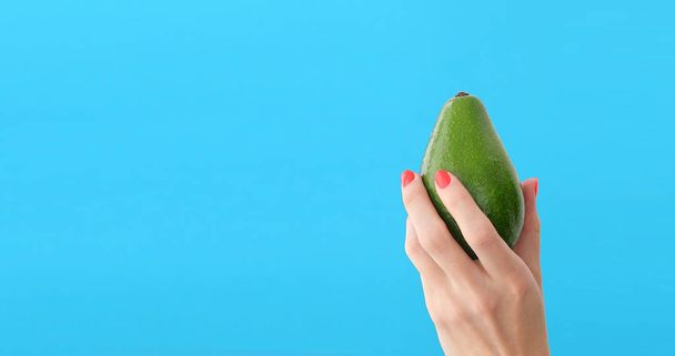 avocado in a hand of woman blue background - Foto, imagen