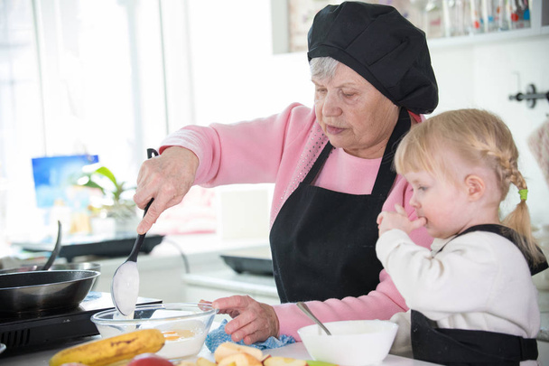 Familia en la cocina. Una niña y su abuela cocinando con una crema agria
 - Foto, Imagen