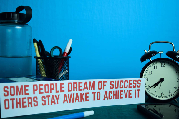 Manche Menschen träumen vom Erfolg, andere bleiben wach, um ihn zu erreichen, und planen ihn vor dem Hintergrund eines Arbeitstisches mit Büromaterial. Geschäftsidee Planung auf blauem Hintergrund - Foto, Bild