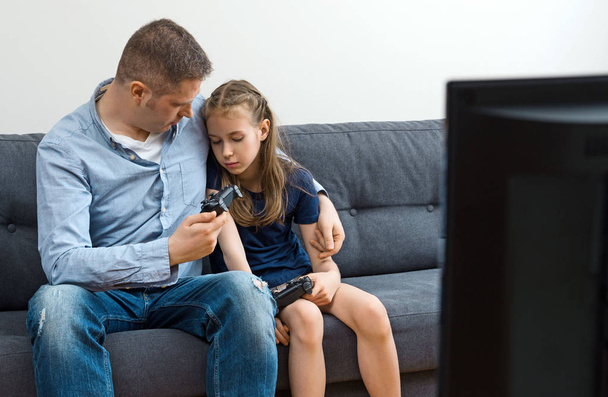 Padre e hija trastornados sentados en el sofá con mandos
. - Foto, imagen