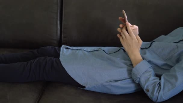 Teenager-Mädchen in blauem Kleid liegt auf einem Sofa und hält ein Smartphone in den Händen. junges Mädchen blättert in den sozialen Medien, Jugendsucht - Filmmaterial, Video