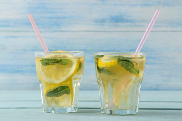 Zelfgemaakte limonade met munt en citroen in plastic glazen op een blauwe houten achtergrond. Verfrissende limonade drankje. - Foto, afbeelding
